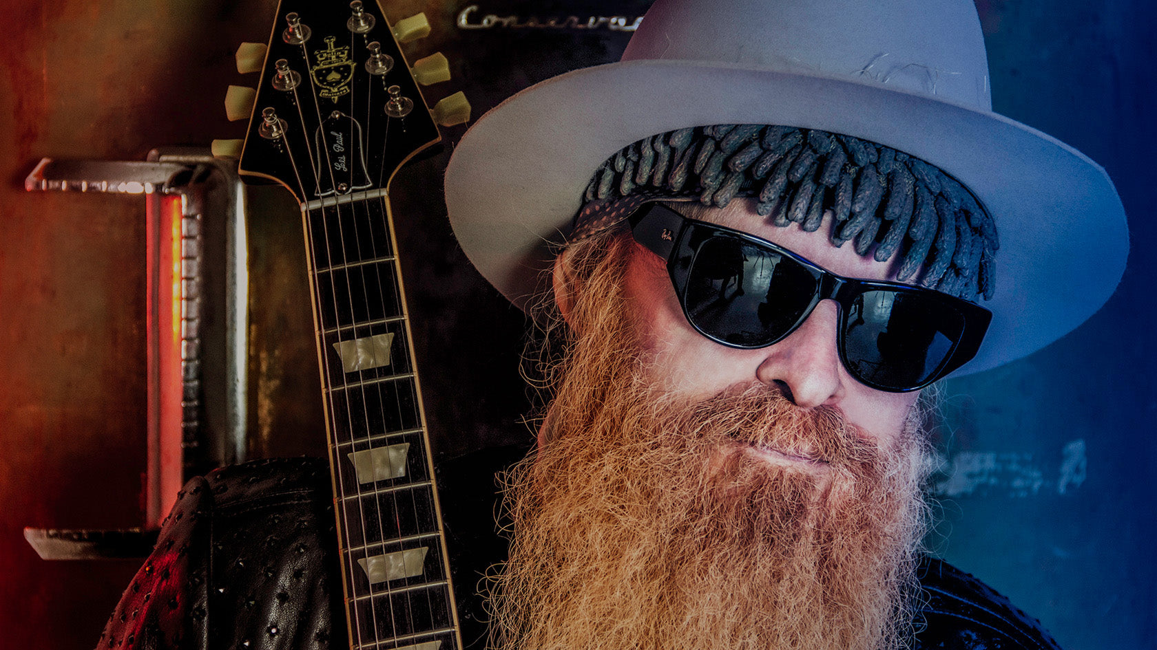 Billy F Gibbons portrait close up wearing hat and sunglasses neck of guitar next to his face