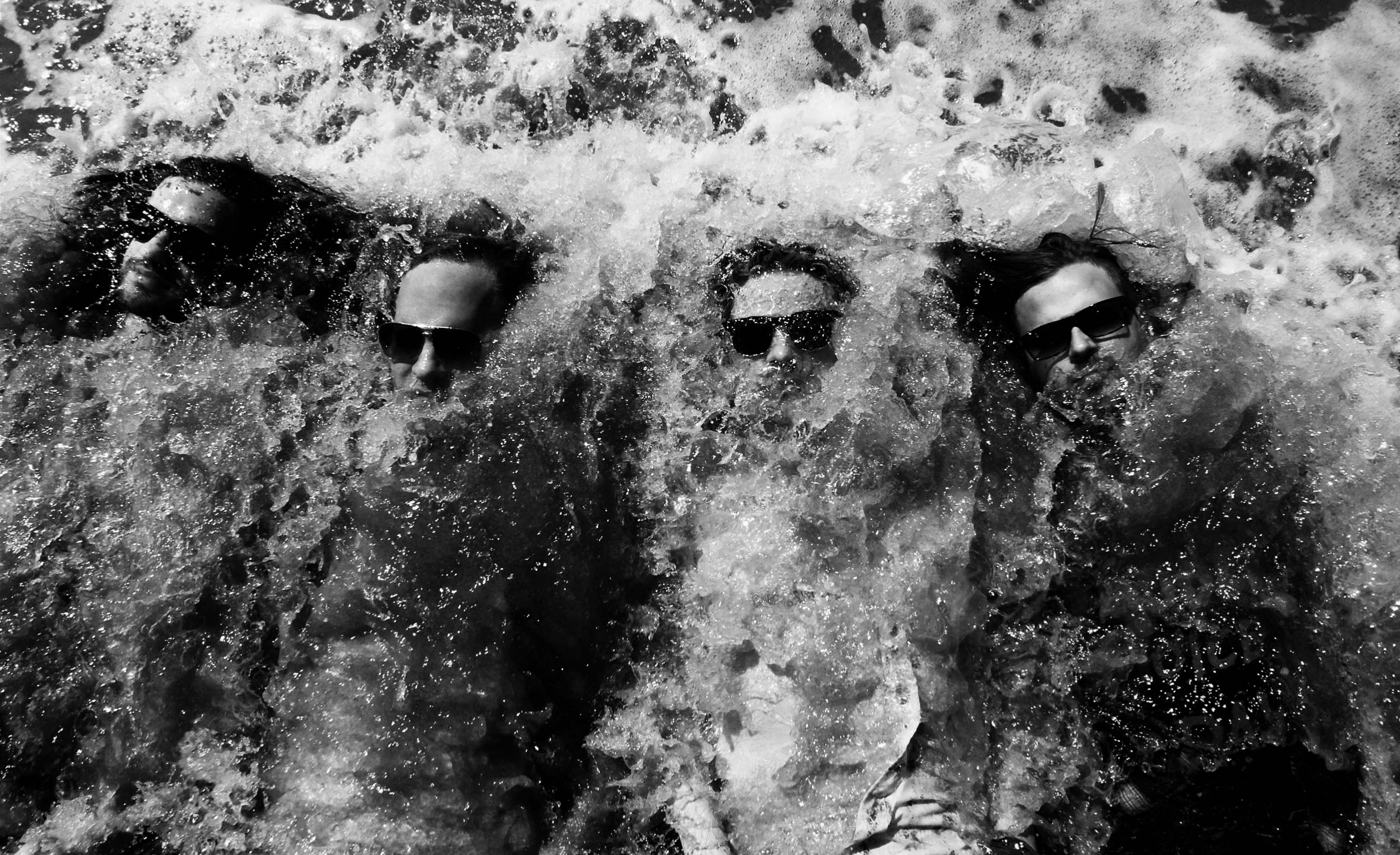 Black and white portrait Venice beach One Bad Son band members immersed in water while wearing sunglasses