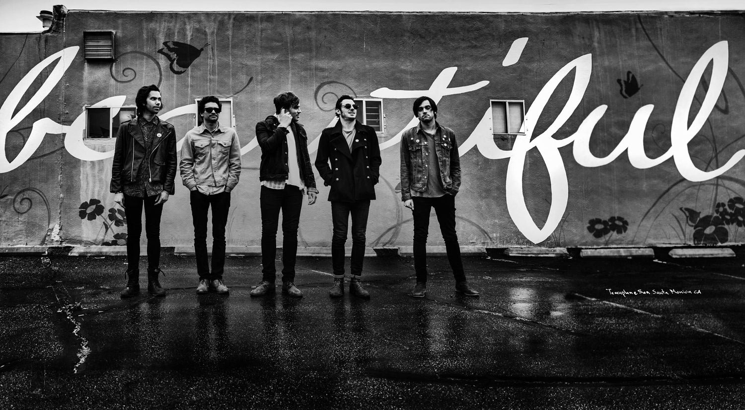 Black and white panoramic image five members Terraplane Sun band standing in front of wall with the word beautiful painted on it in script