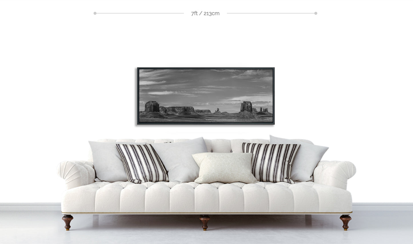 Monument Valley metal panoramic fine art print displayed above white sofa with patterned cushions against white wall