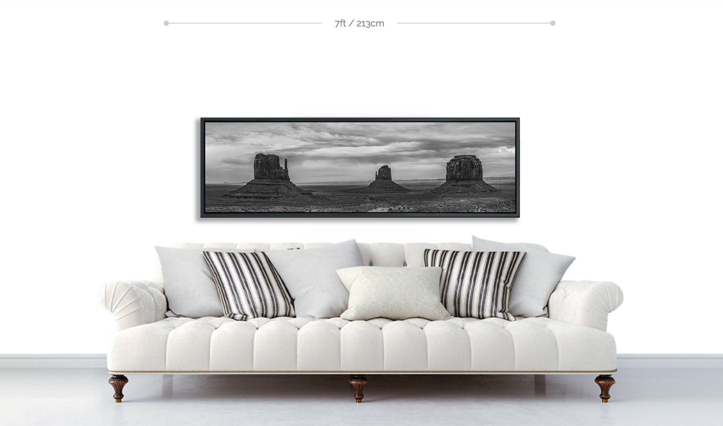 Monument Valley panoramic metal print displayed hanging above white sofa with patterned pillows