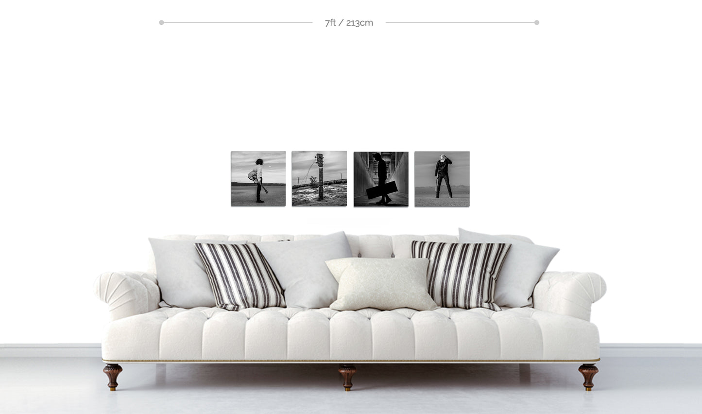 Set of four black and white fine art square metal prints arranged in horizontal line on white wall above white sofa with cushions