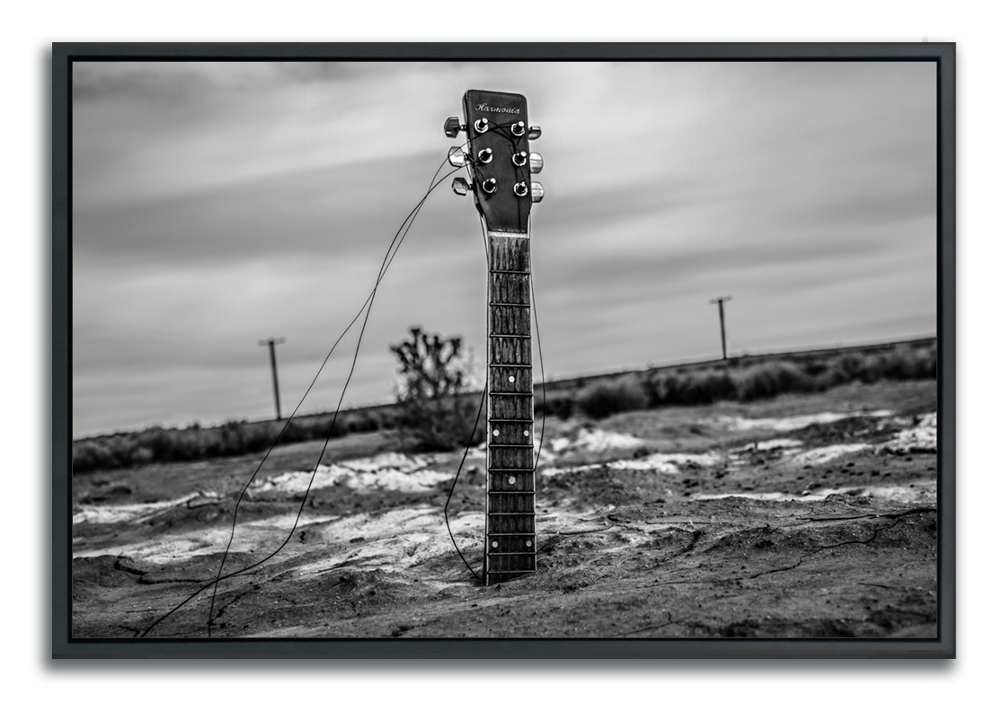 Black and white framed fine art photograph guitar neck protruding from body buried in desert sand