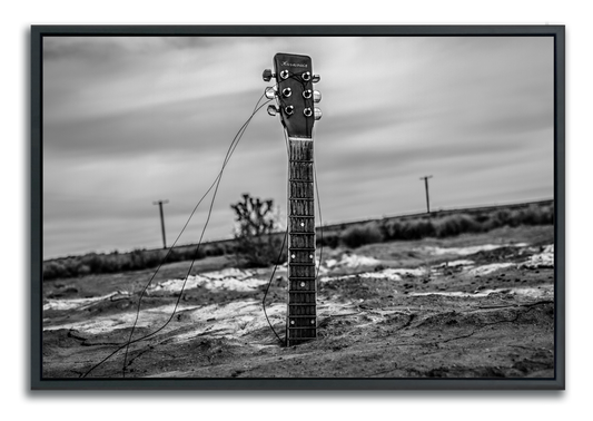 Black and white framed fine art photograph guitar neck protruding from body buried in desert sand