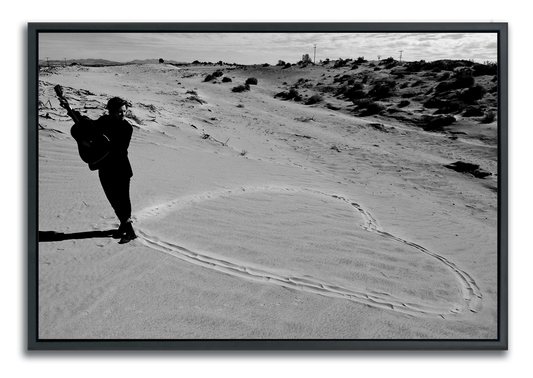 Black and white fine art photography men standing with guitar at the pint of a heart drawn in sand