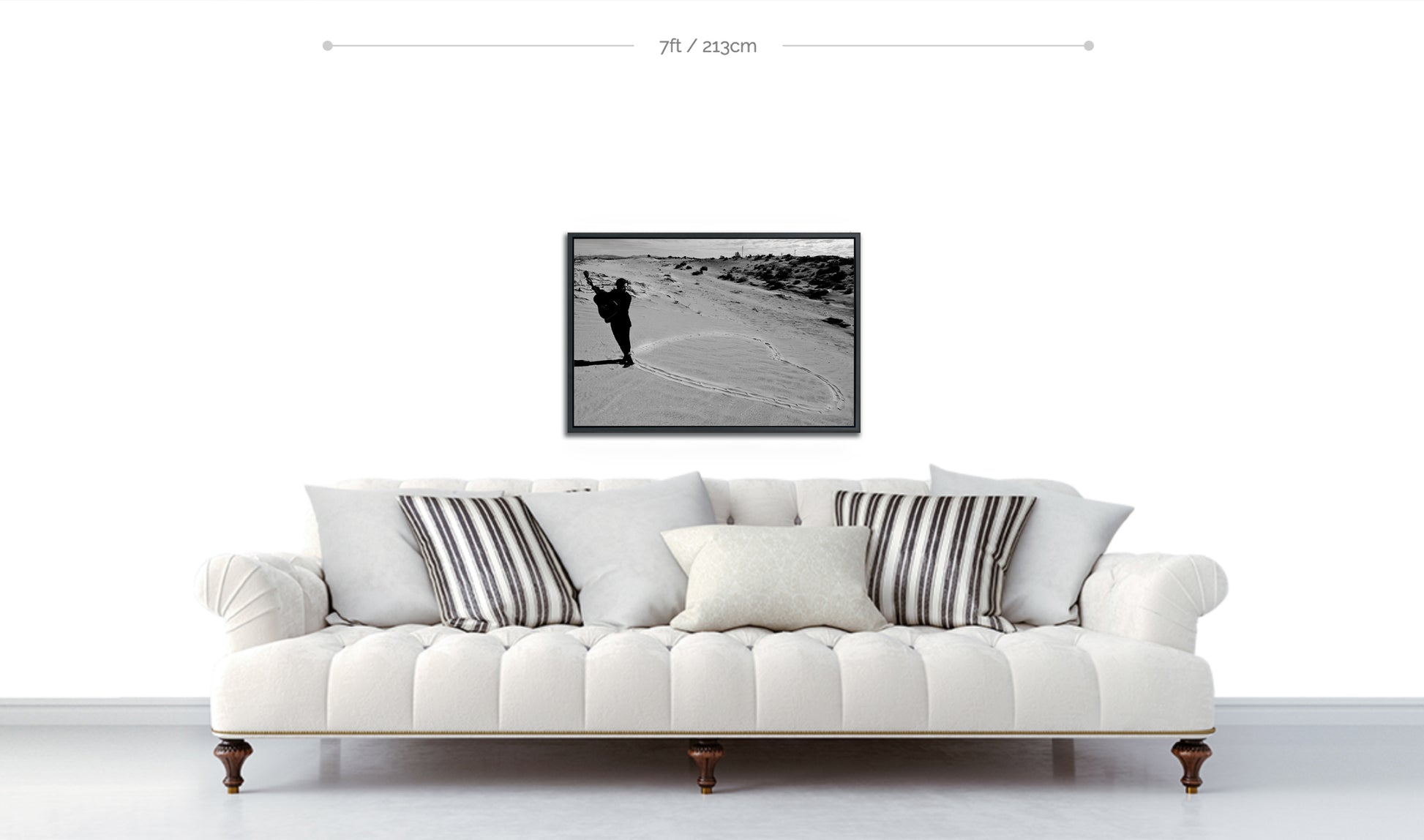 Framed black and white metal print of musician holding guitar at the point of a heart drawn in the sand displayed hanging above white sofa