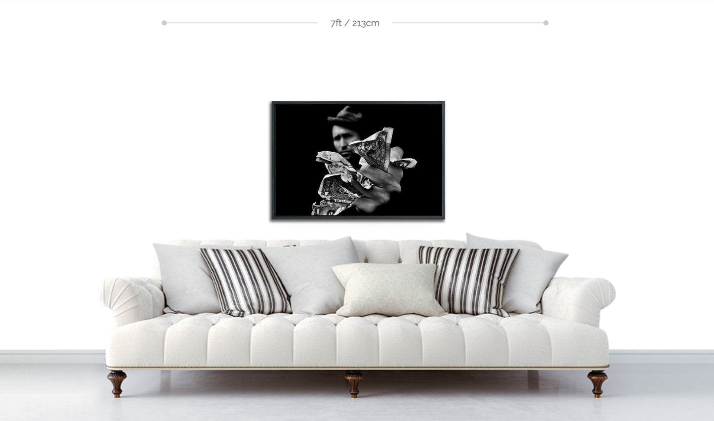 Framed black and white fine art photograph displayed above sofa man wearing hat out of focus in background with hand outstretched holding fistful of money in foreground