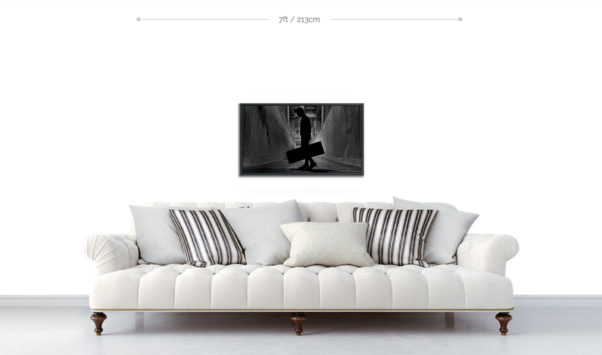 Fine art black and white metal framed print displayed above white sofa on white wall silhouetted man holding guitar case in tunnel under bridge