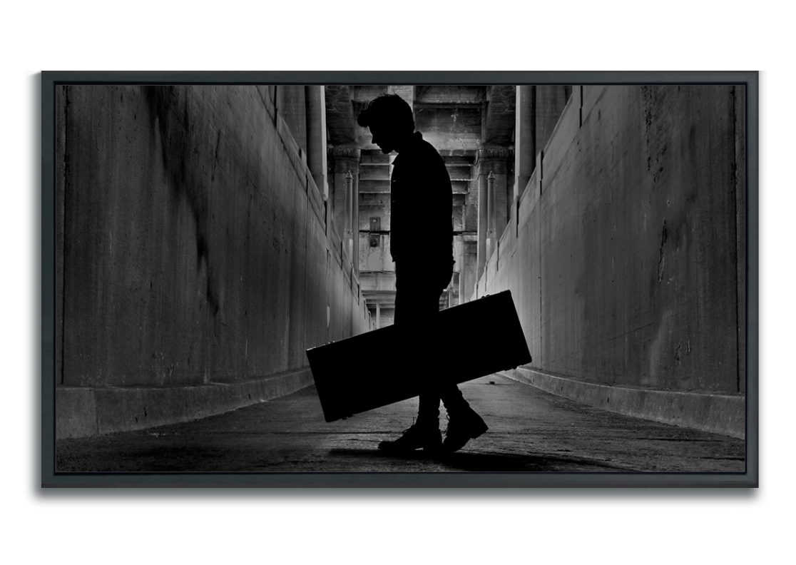 Black and white fine art photographic metal print framed silhouetted man holding guitar case in tunnel under bridge